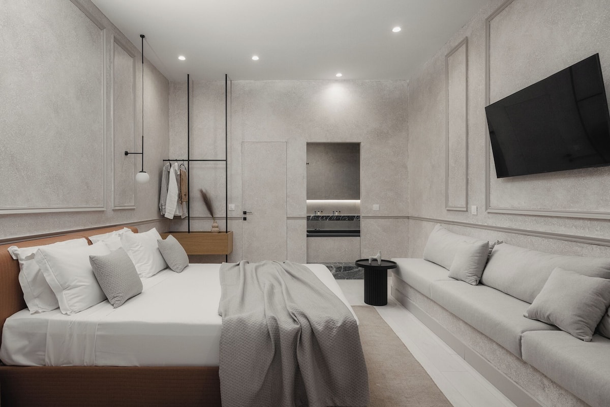 Une chambre moderne avec un lit, un canapé, une télévision et une salle de bain visible à travers une porte.
