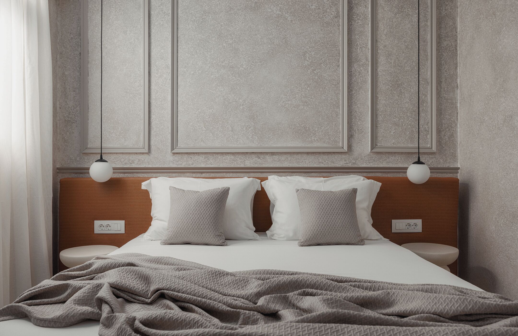 A neatly made bed with a grey blanket, two white pillows, and a wooden headboard. There are two bedside tables with white lamps.