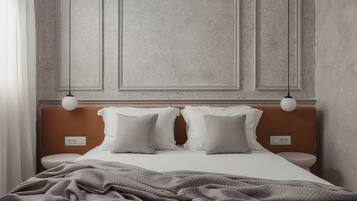 A neatly made bed with a grey blanket, two white pillows, and a wooden headboard. There are two bedside tables with white lamps.