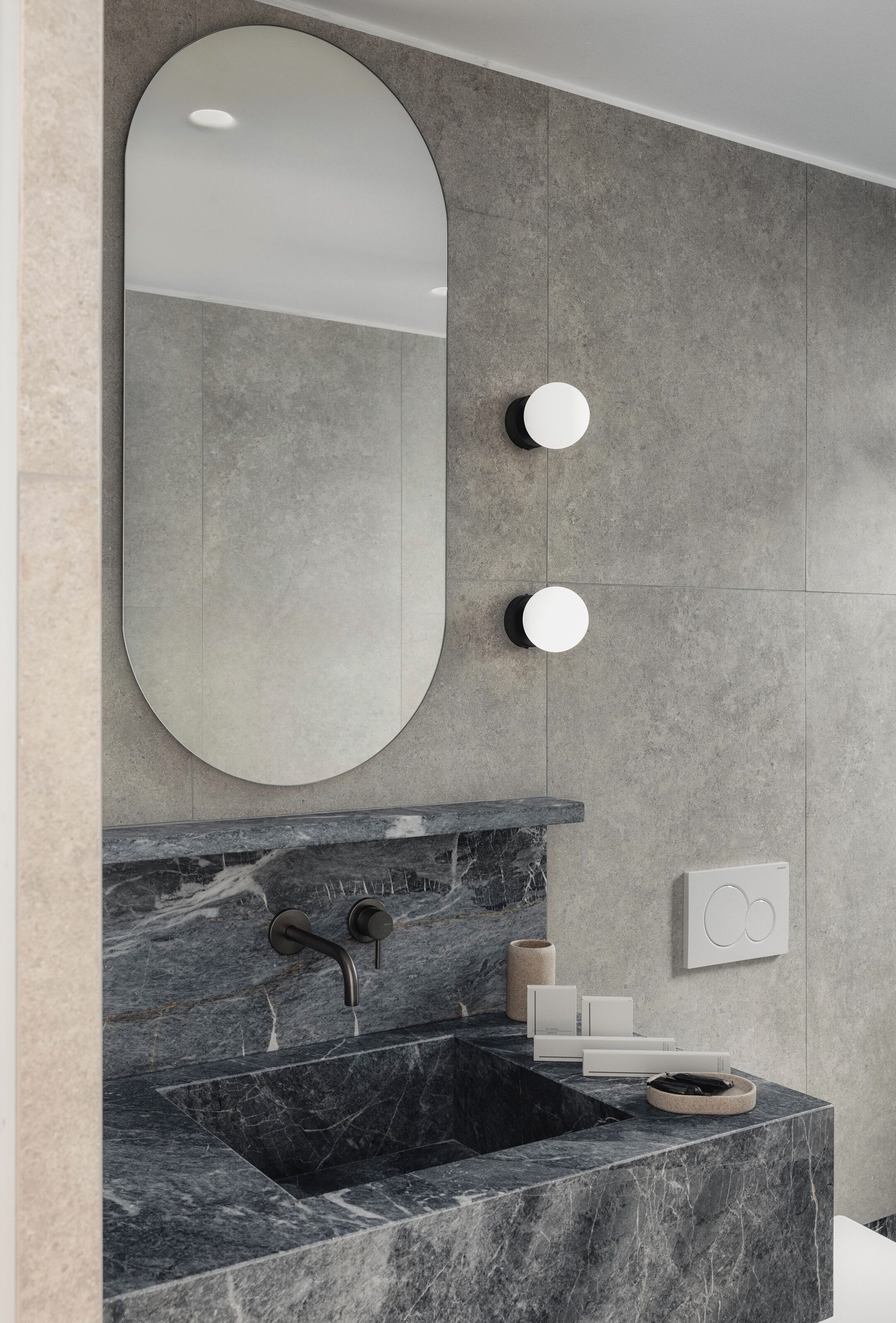 Un baño moderno con un lavabo de mármol, un espejo grande y dos apliques de pared redondos.