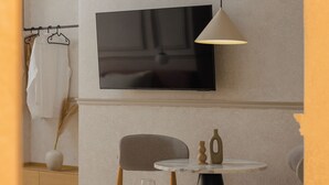 Une chambre moderne avec un téléviseur à écran plat fixé au mur, une table ronde avec deux chaises, un petit vase et un verre à vin posés sur la table.