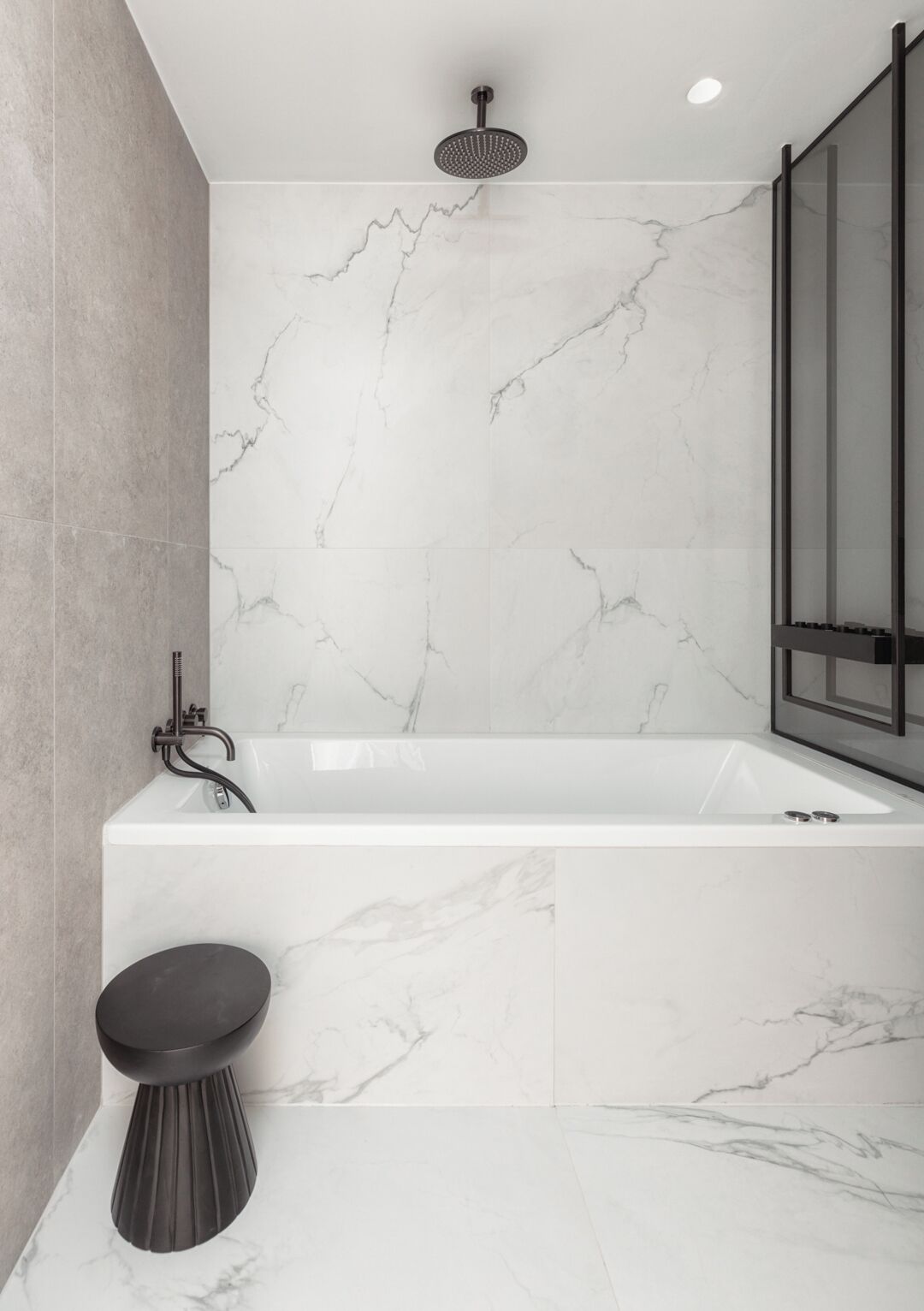 A modern bathroom with a marble wall, a freestanding bathtub, and a black pedestal sink.
