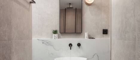 Un baño moderno con lavamanos de mármol, un espejo grande e iluminación empotrada.