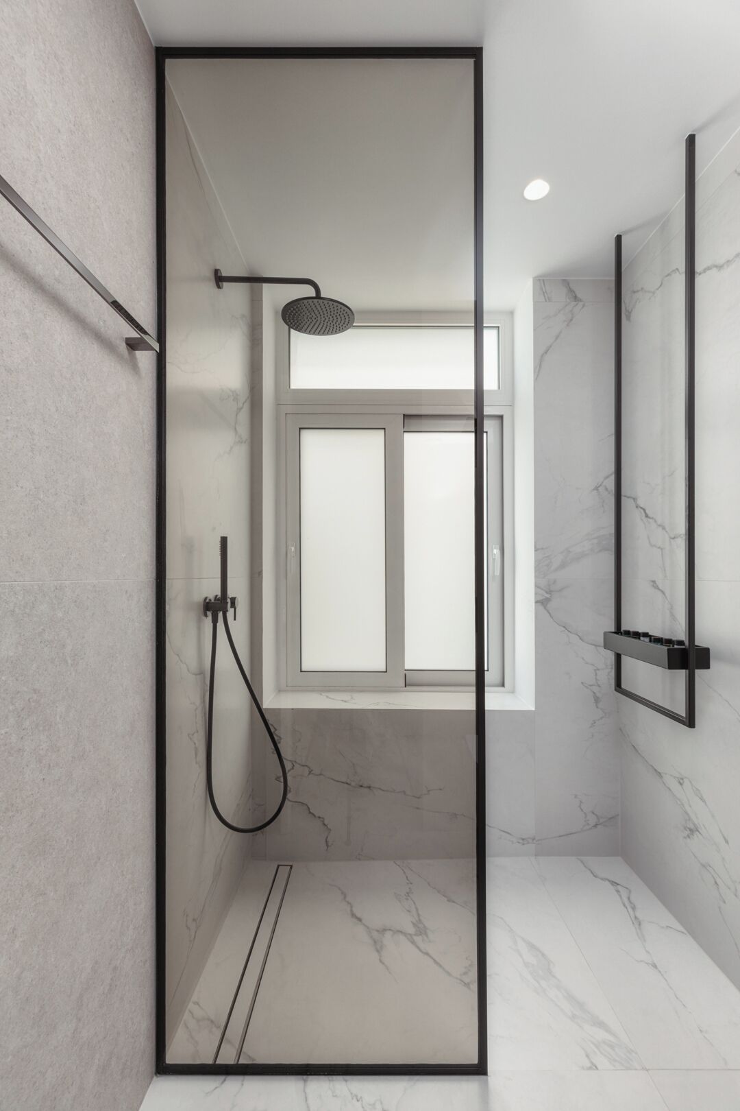 Ein modernes Badezimmer mit einer Duschkabine aus Glas, einer Handbrause und einem Marmorboden.