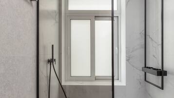A modern bathroom with a glass shower enclosure, a handheld showerhead, and a marble floor.