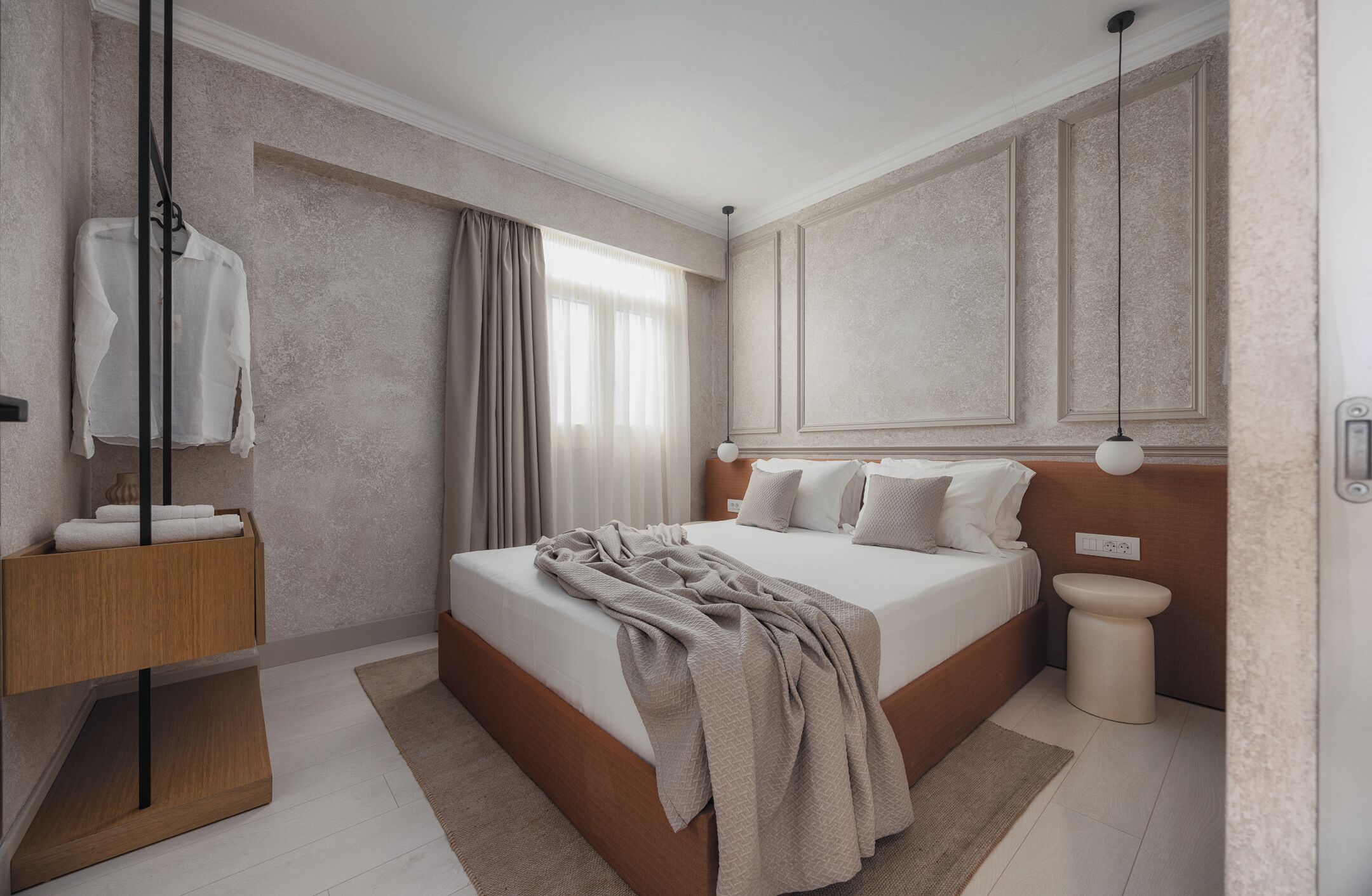 Une chambre moderne avec un grand lit, une table de chevet en bois, un luminaire suspendu et une vue sur la salle de bain.