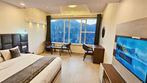 Une chambre d’hôtel avec un grand lit, un bureau, une chaise, une télévision et une fenêtre donnant sur la montagne.