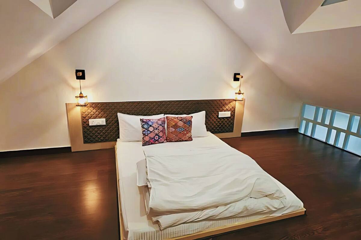 A bedroom with a sloped ceiling, a bed with white linens, a quilted headboard, and two wall-mounted lights.
