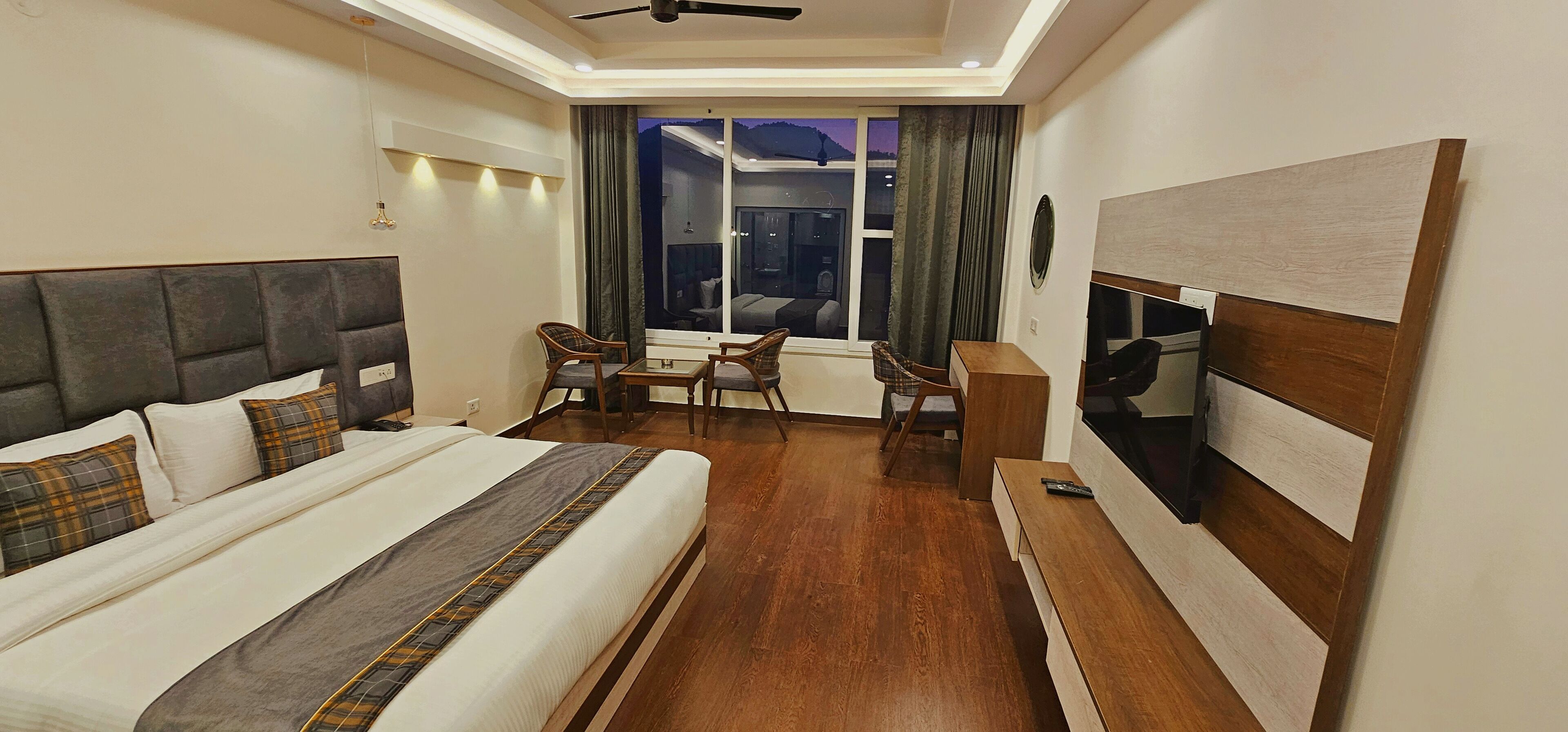 A hotel room with a large bed, a desk, two chairs, a TV, and a view of the outdoors.