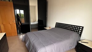 Camera da letto con un letto, un comodino, una cassettiera e una porta scorrevole che dà su un'altra stanza.