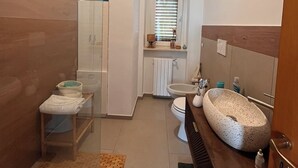 Un bagno moderno con doccia in vetro, vaso sospeso e lavabo freestanding.