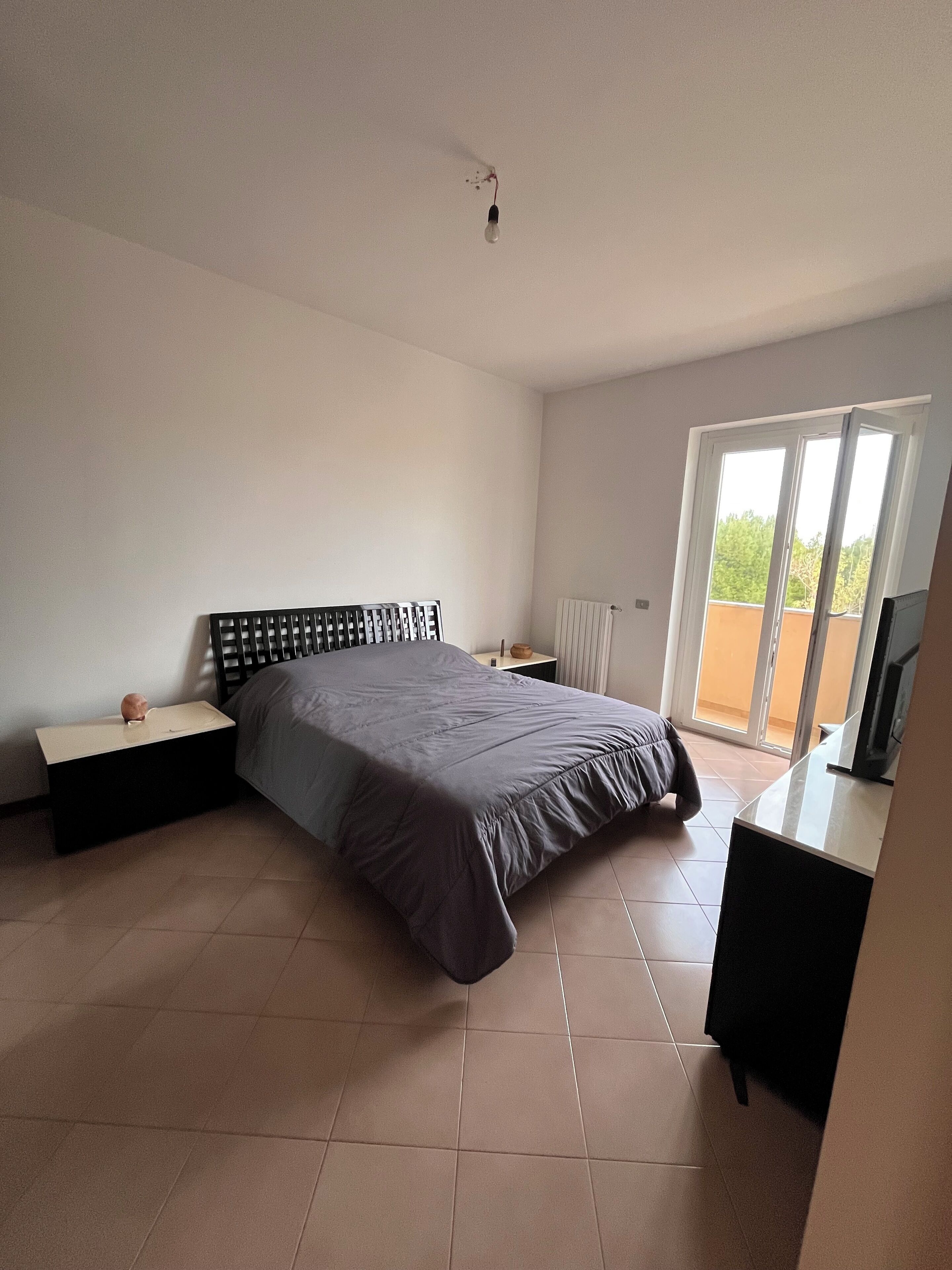 A bedroom with a bed, a nightstand, a dresser, a radiator, and a sliding glass door to the outside.