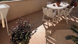 Un balcone illuminato dal sole con un tavolo e sedie, una pianta in vaso e vista sulla campagna.