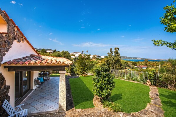 Un patio con mobiliario exterior, un muro de piedra y vistas al paisaje costero.