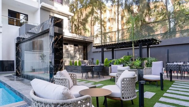 Un patio moderno al aire libre con piscina, mobiliario de mimbre y una pérgola.