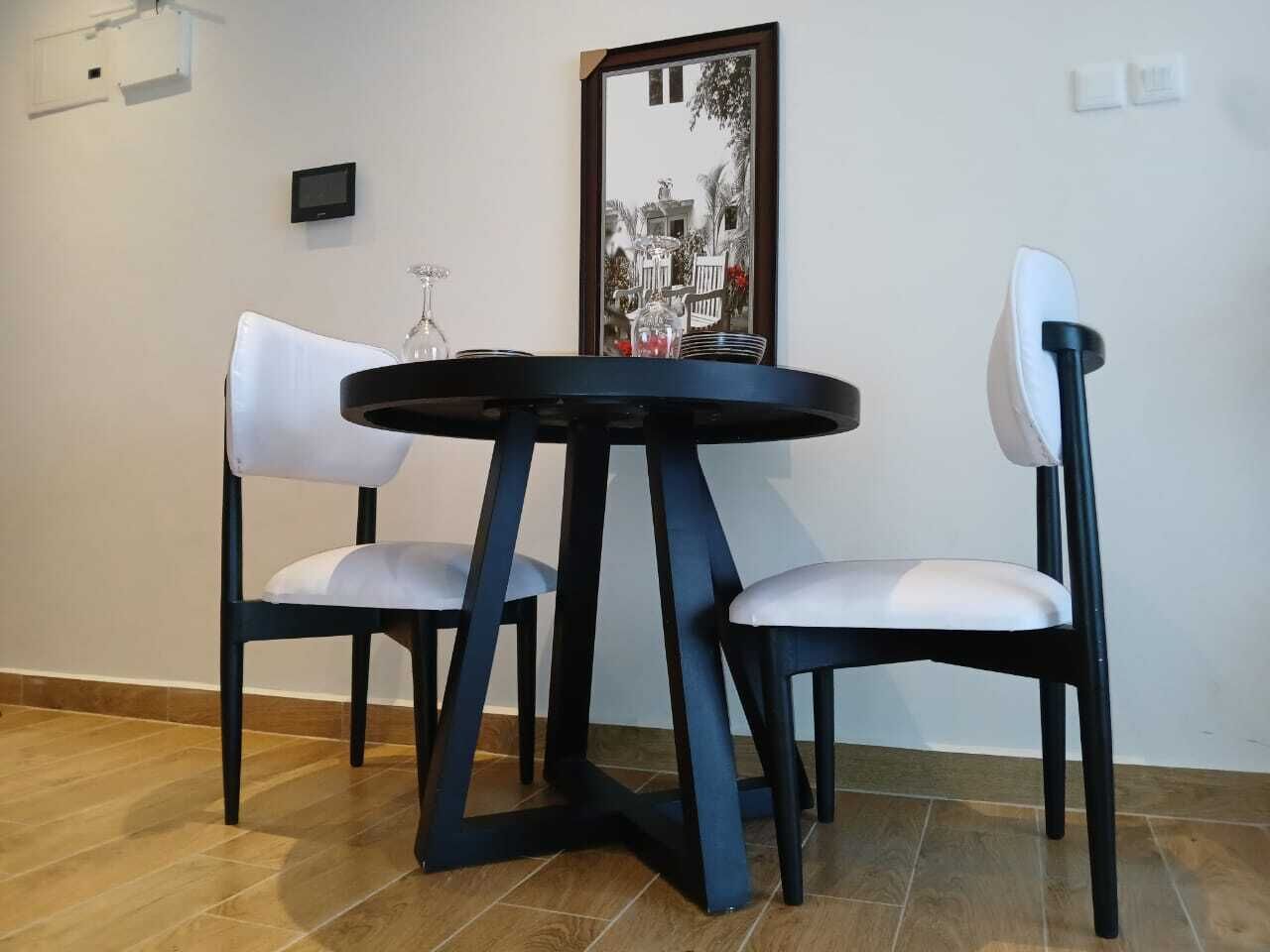 A dining area with a round table and two chairs, a framed picture on the wall, and a small screen above the table.