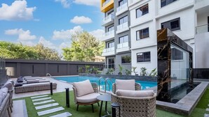 Un área de piscina moderna al aire libre con mobiliario de salón y una sección con paredes de cristal.