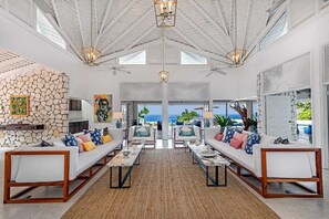 A spacious living area with a stone wall, two sofas with colorful cushions, a coffee table, and a view of the ocean. - Eden Estate (Montego Bay)