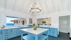 Una cocina moderna con armarios azul claro, una isla blanca y un amplio ventanal con vista al océano.