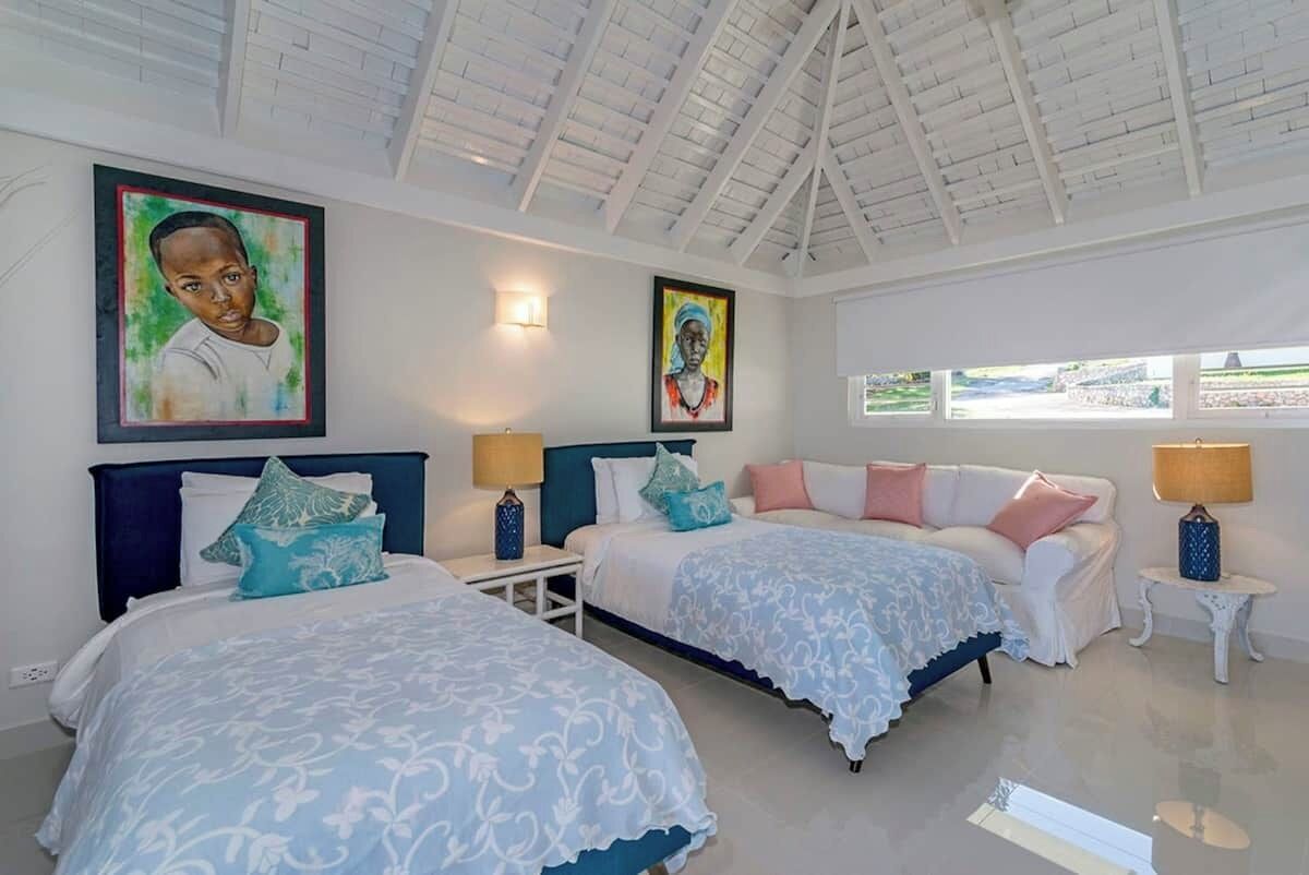 A hotel room with two beds, a white sofa, and artwork on the walls.