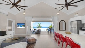Amplia sala de estar con vista al océano, comedor con sillas rojas y cocina moderna.