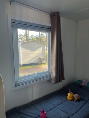 A room with a window overlooking a trailer, a bed with a blue mattress, and a stuffed toy on the bed. - Bungalow 4-6 personnes Dunes de Contis (Saint-Julien-en-Born)