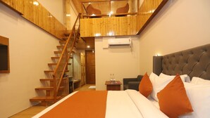 A bedroom with a large bed, a wooden staircase, a small table with bottles, and a chair. - Udit Regency by west western kasol ( Central Heated and Air Cooled ) (Bhuntar)
