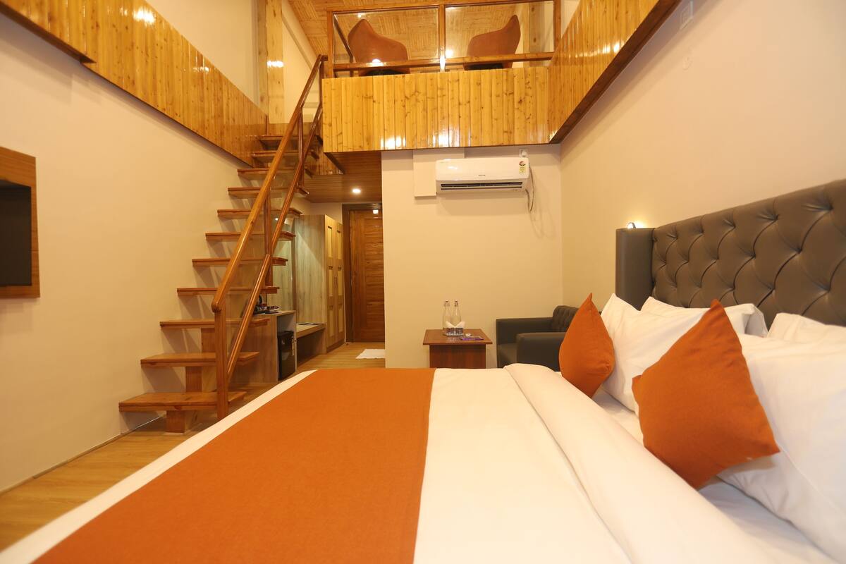 Ein Schlafzimmer mit einem großen Bett, einer Holztreppe, einem kleinen Tisch mit Flaschen und einem Stuhl.