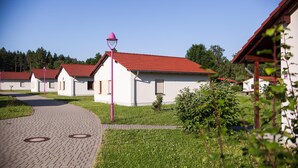 A row of white buildings with red roofs, a paved walkway, and a small green area with bushes.