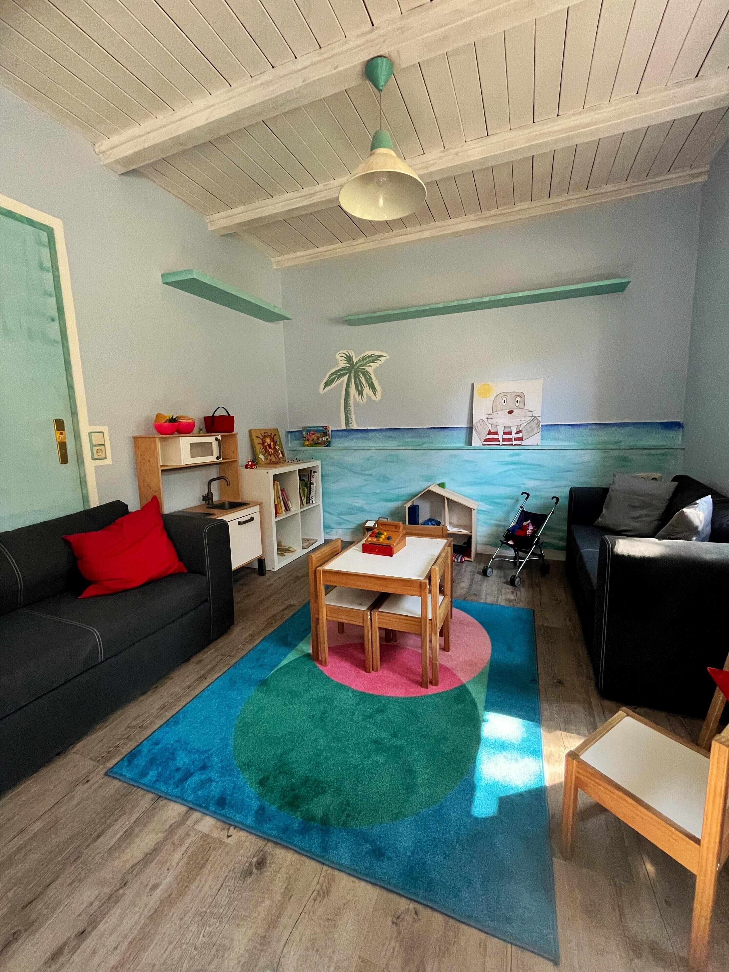 A living room with a wooden table, two sofas, a colorful rug, and a wall mural of a beach scene.