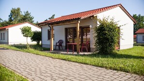 A small, single-story building with a red-tiled roof and a covered patio area with two chairs and a table.