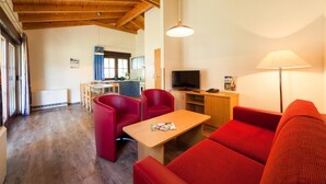A cozy living room with a wooden ceiling, a TV, a red sofa, and a dining area in the background.
