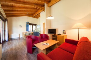 Una sala de estar acogedora con techo de madera, un televisor, un sofá rojo y una zona de comedor al fondo.