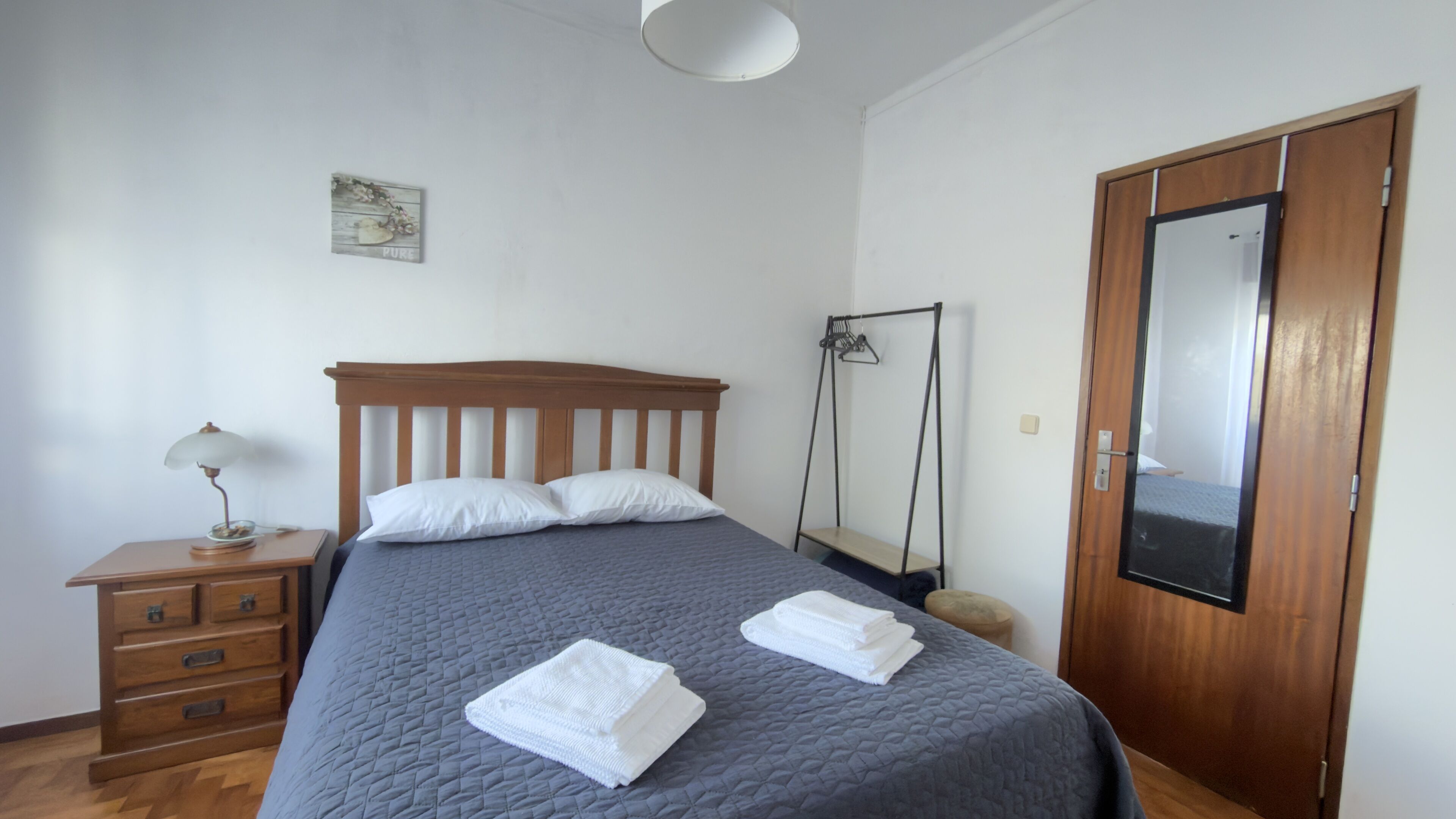 Ein Schlafzimmer mit einem Bett, einem Nachttisch aus Holz, einer Lampe, einer Pendelleuchte, einem Kleiderschrank und einem an der Wand befestigten Bild.