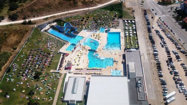 Vista aérea de un complejo turístico con varias piscinas, un amplio estacionamiento y un edificio con techo plano.
