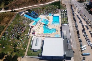 Luchtbeeld van een resort met meerdere zwembaden, een groot parkeerterrein en een gebouw met een plat dak.