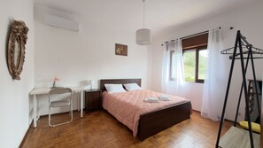 Quarto com cama, escrivaninha, cadeira, luminária pendente e janela com cortinas.