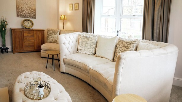 A living room with a white sofa, a wooden cabinet, a lamp, and a window with curtains.