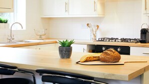 A modern kitchen with white cabinets, a wooden countertop, a gas stove, and a loaf of bread on the counter.