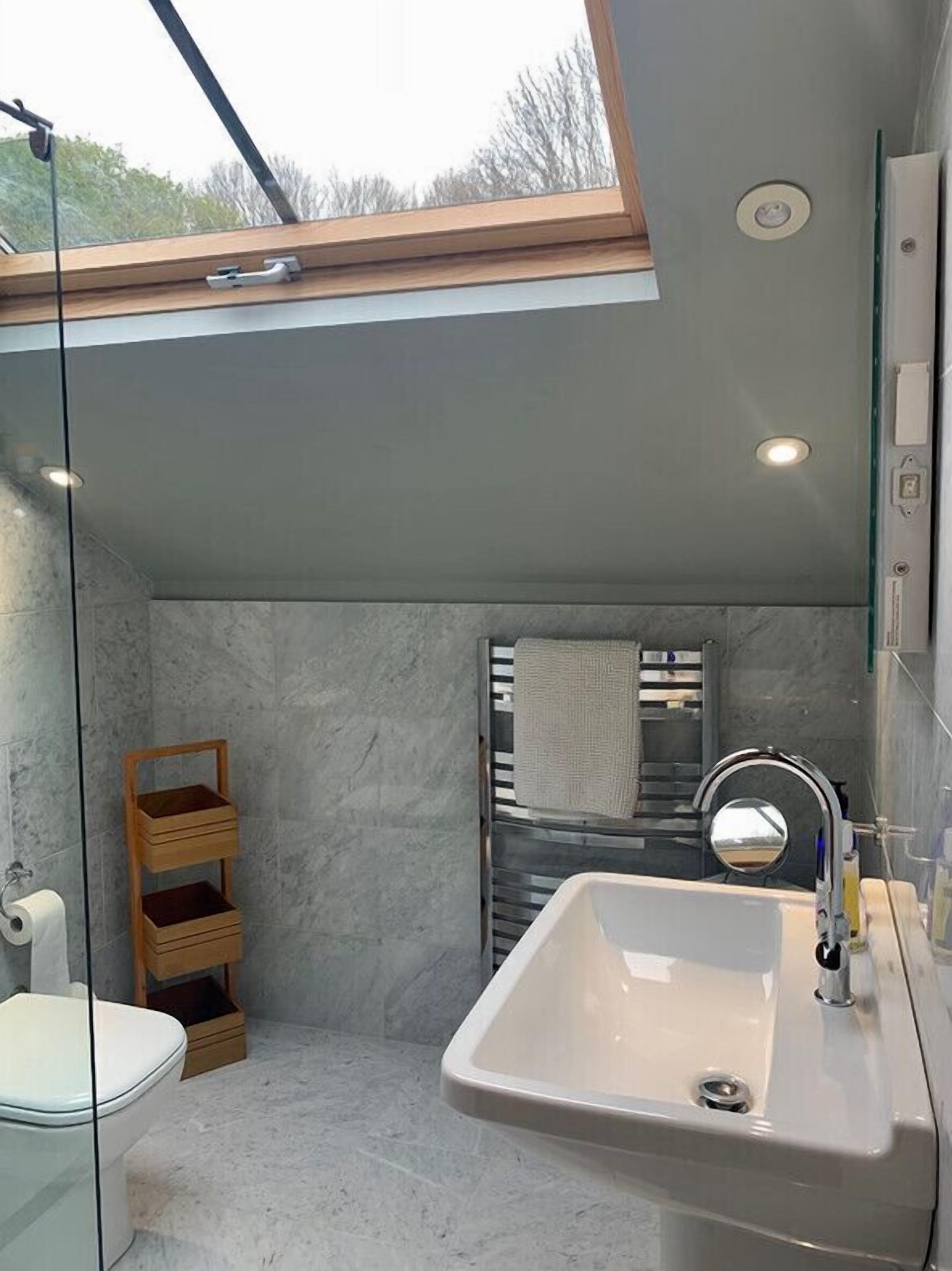 A compact bathroom with a skylight, a white sink, and a wooden storage unit.