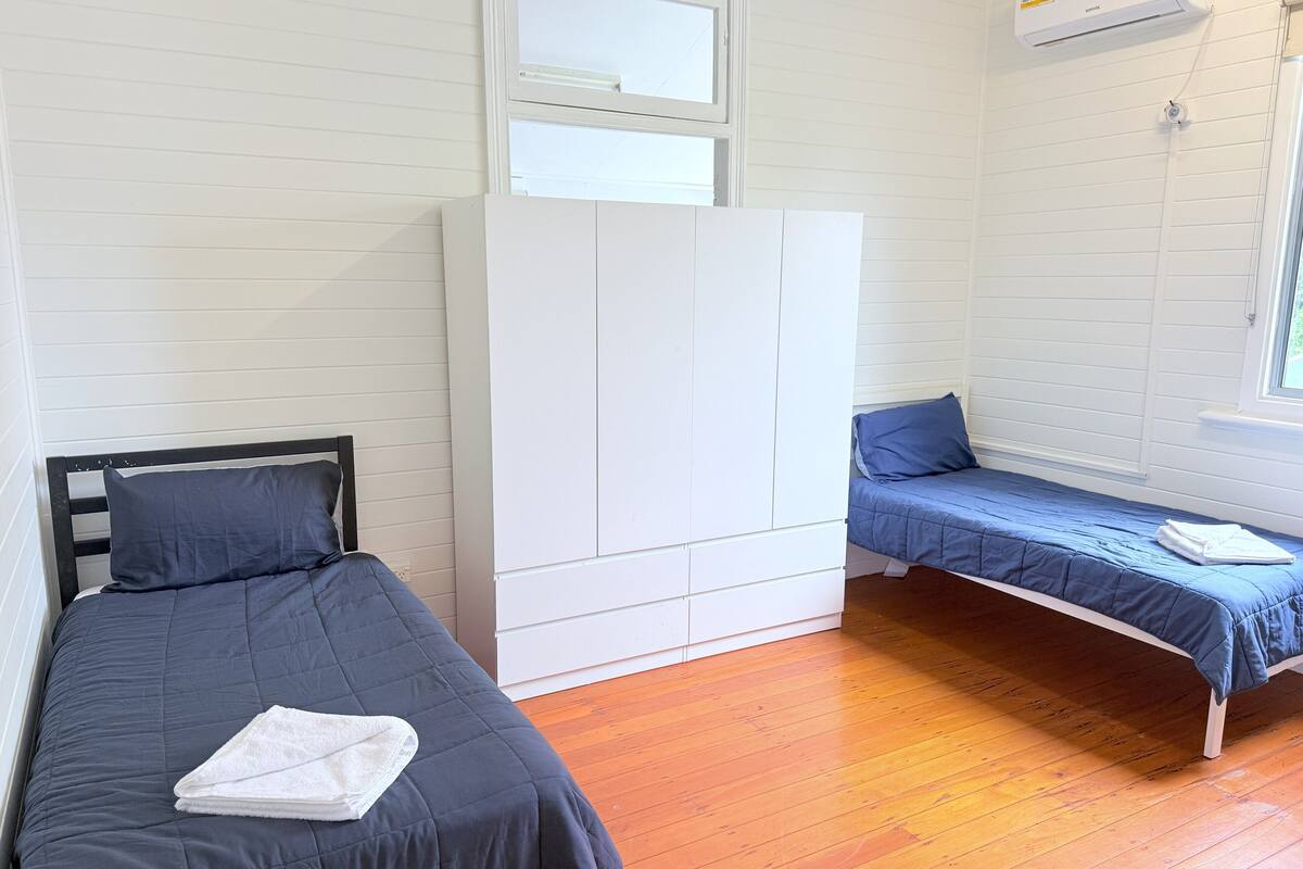 Une chambre avec deux lits simples, une armoire blanche et un appareil de climatisation.