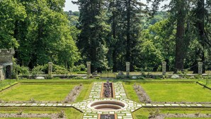 Een formele tuin met een middellange pad, stenen elementen en weelderige begroeiing.