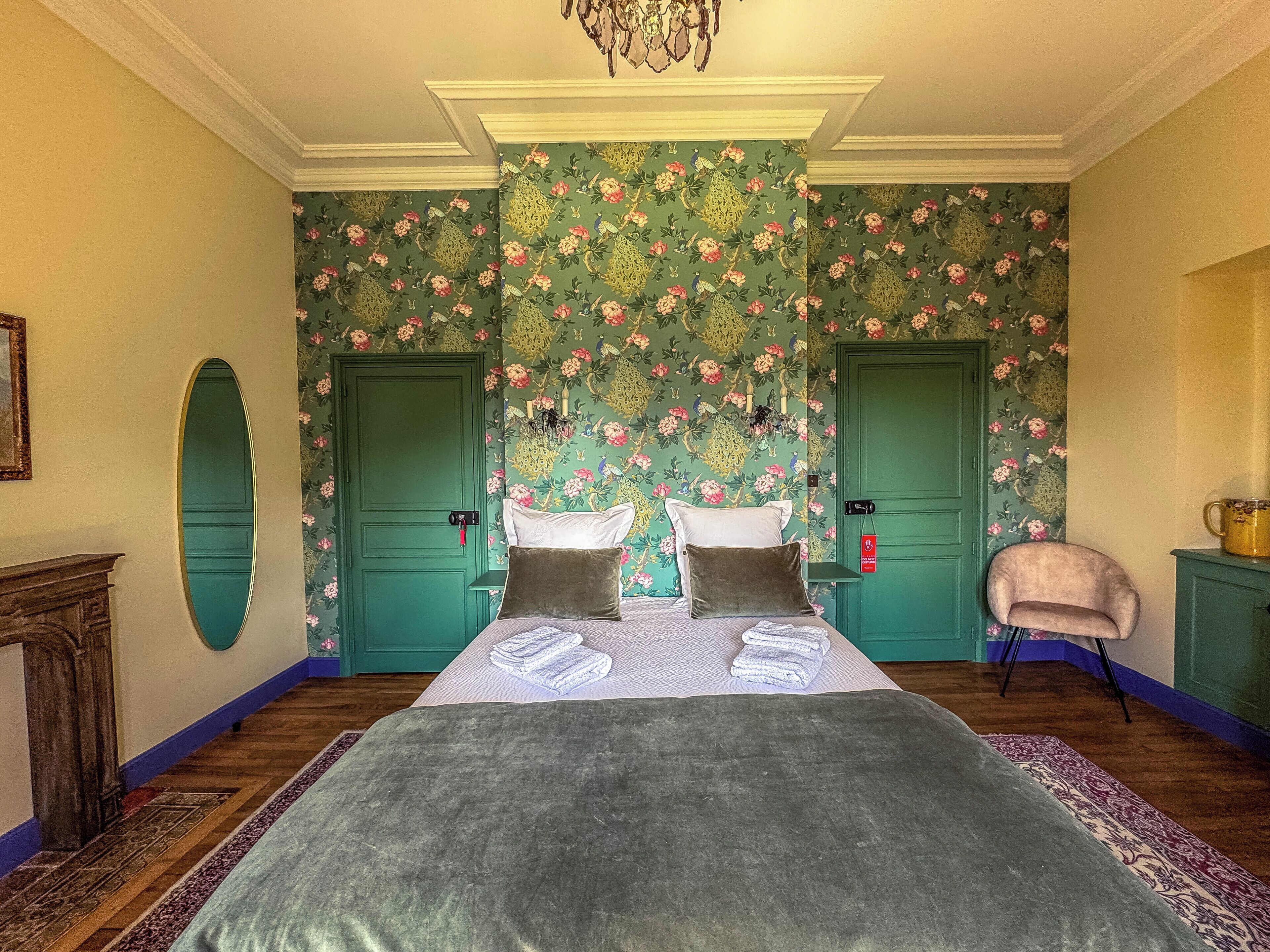 Une pièce avec un grand lit, deux portes, une chaise et une cheminée.