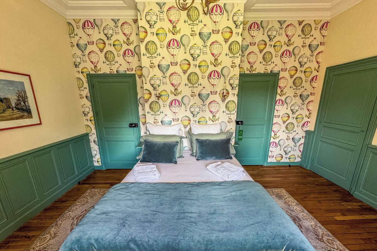 Een slaapkamer met een groot bed, twee groene deuren en behang met luchtballonmotieven.
