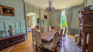 Een eetkamer met een houten tafel en stoelen, decoratieve sierlijsten en een kroonluchter.