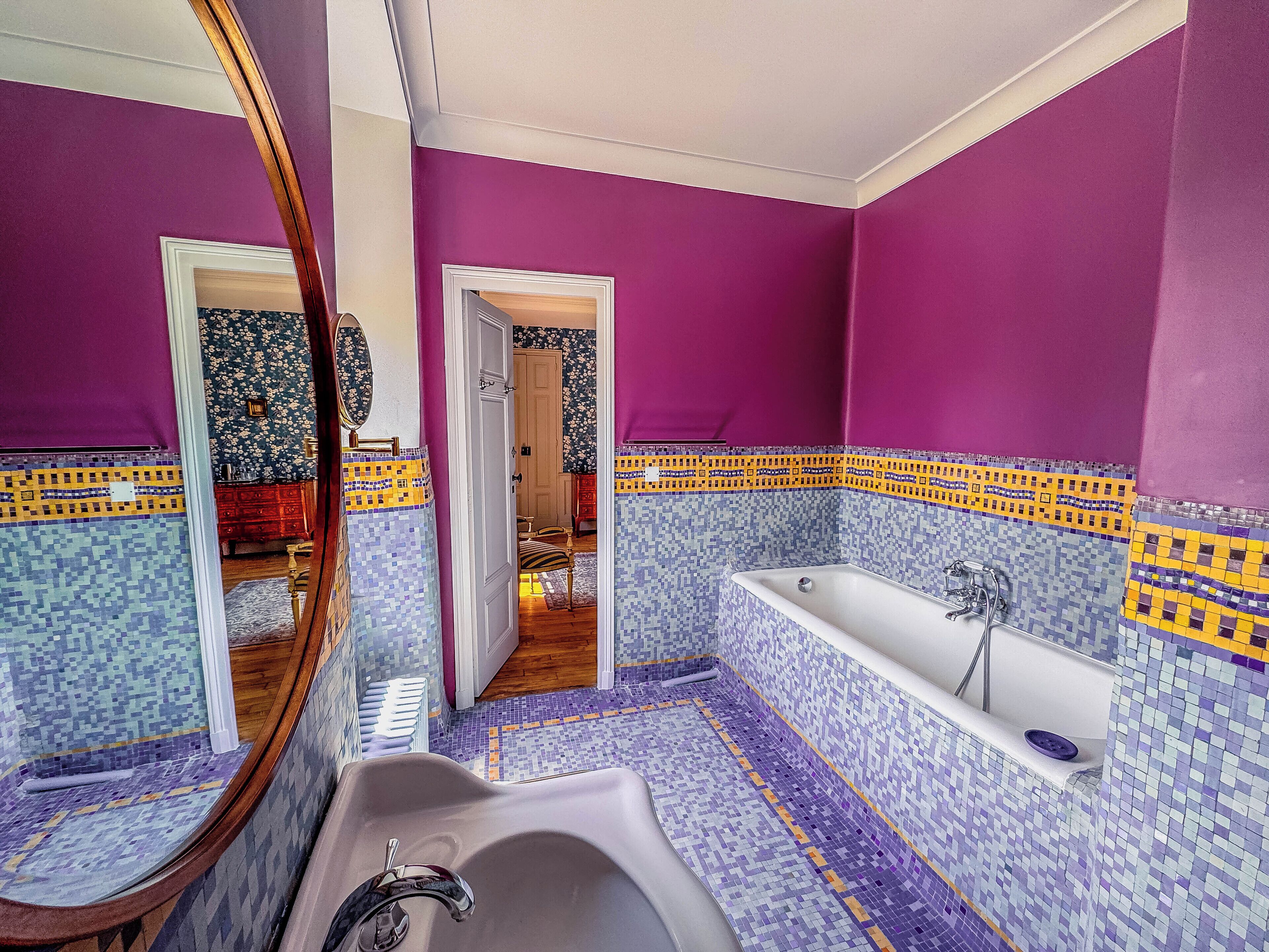 Casa de banho com paredes roxas, chão em mosaico e uma banheira.