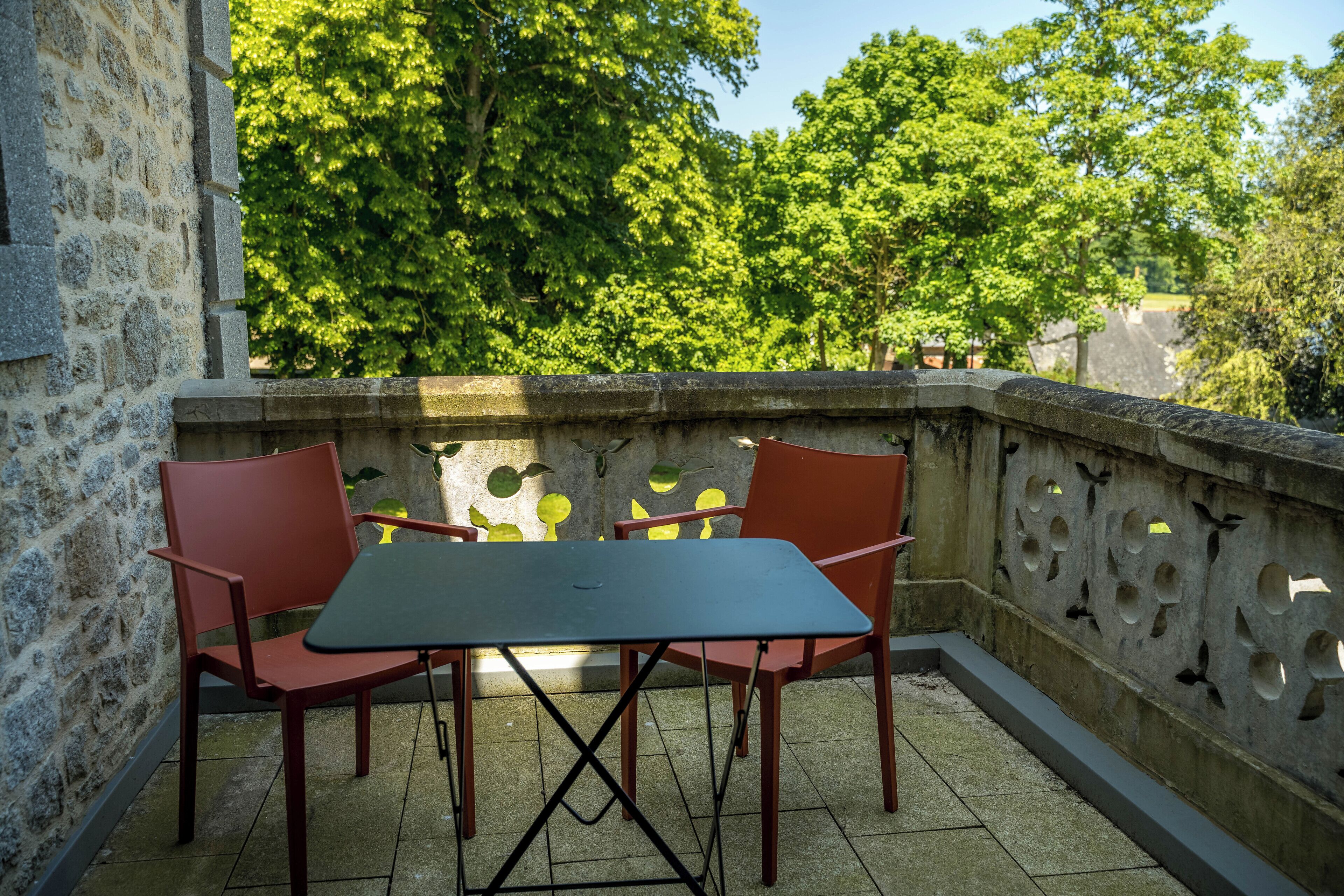 Un balcon avec un mur en pierre, deux chaises rouges et une table.