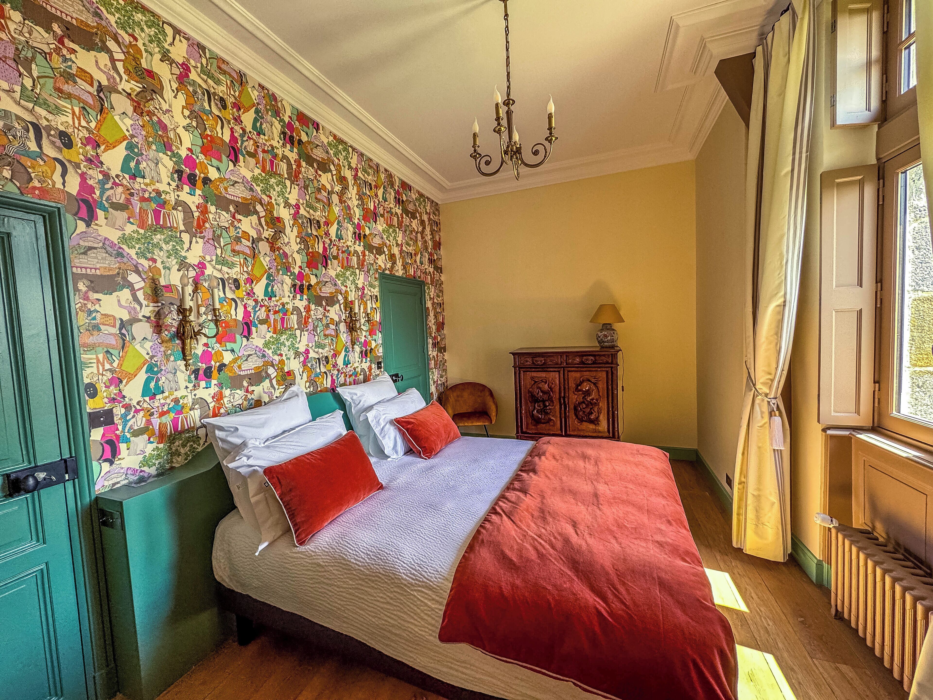 Un dormitorio con una cama grande, una mesita de noche verde, un armario de madera y una pared con un mural colorido.