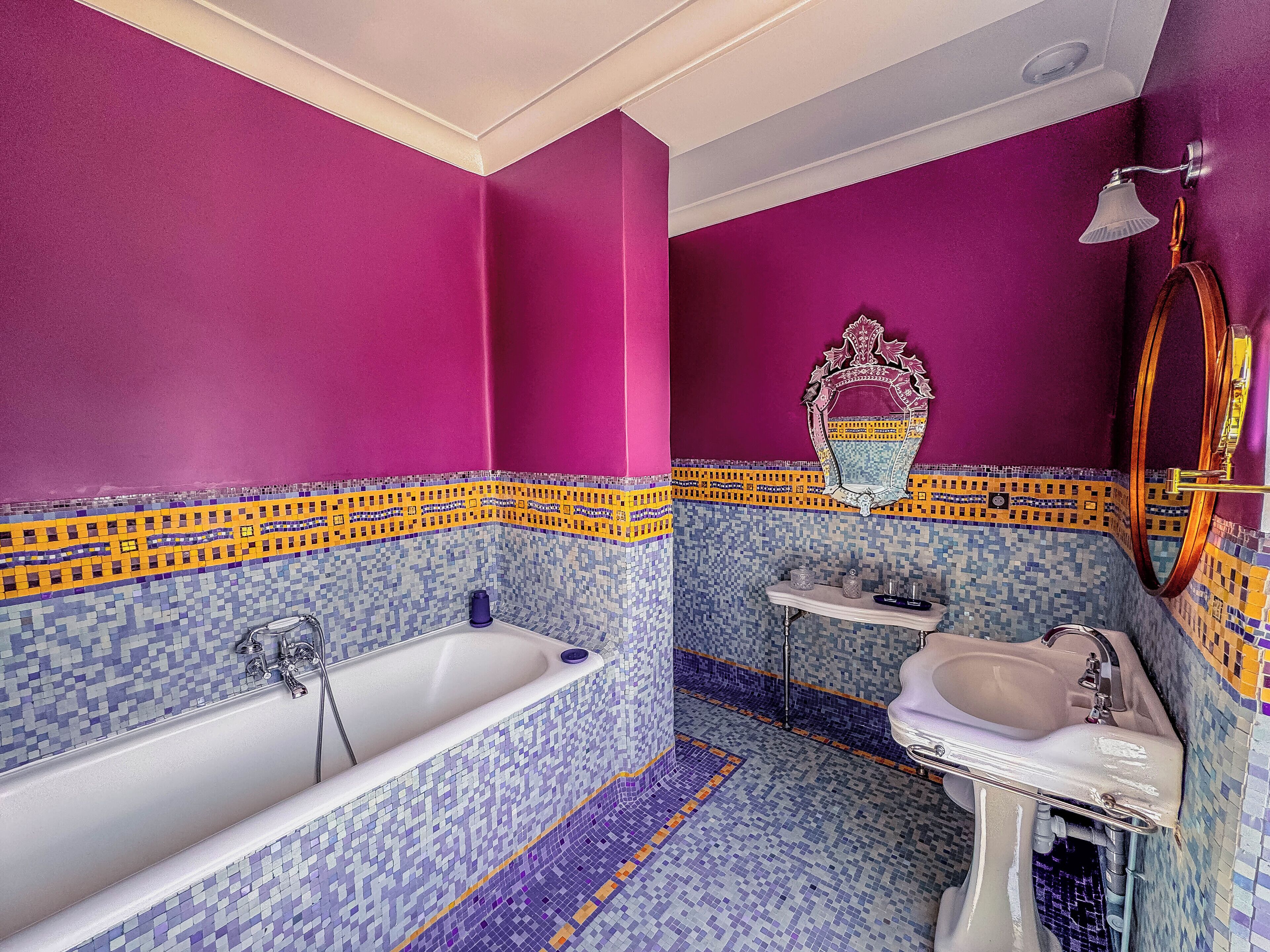 A bathroom with a white bathtub, a sink, and a mirror. The walls are painted in bright pink, and the floor has a mosaic tile design.