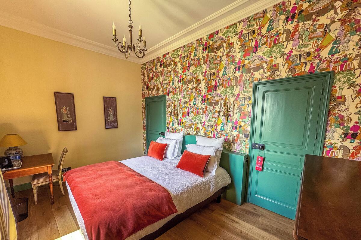 Een slaapkamer met een bed, een bureau, een stoel en een groene deur.